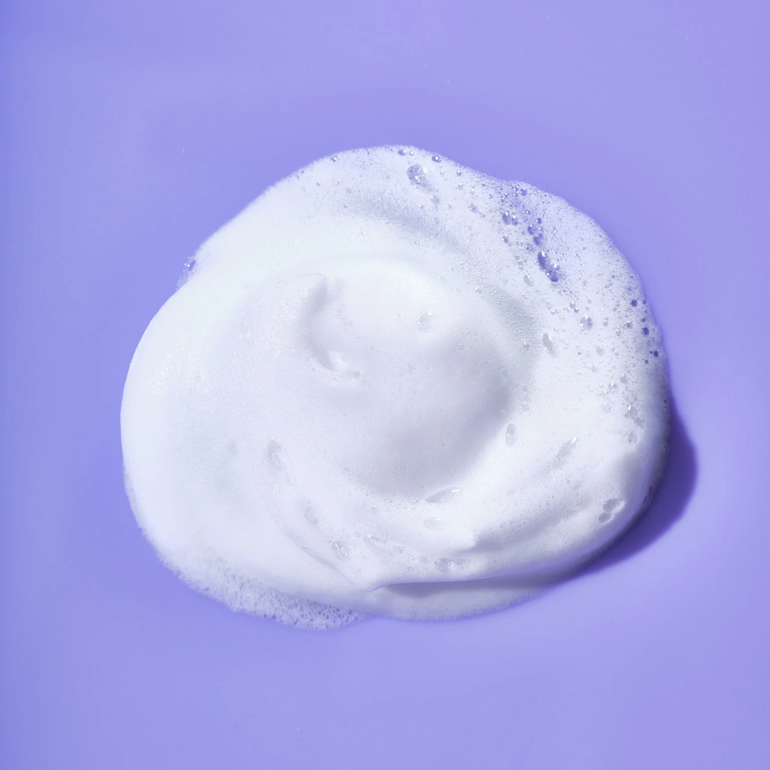 A fluffy white foam bubble from Good Molecules Acne Foaming Cleanser with Salicylic Acid BHA contrasts against a smooth purple background, highlighting the soft texture of the foam and the vibrant color behind it.