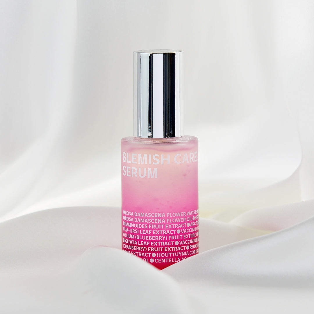 ISOI Blemish Care Serum in a pink gradient bottle with a silver cap, placed on white satin fabric. Formulated with Bulgarian Rose Oil for brightening and blemish care.