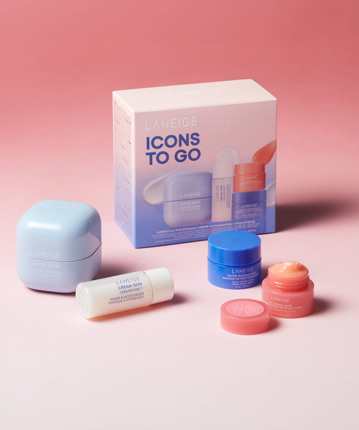 Laneige Icons To Go - 4 Piece set against a pink background, featuring a hydrating mini essentials set with blue water bank hyaluronic acid moisturizer, white cream skin toner, blue sleeping mask, and two small containers with orange and rose-tinted lids. Packaging box labeled Icons to Go in the background.