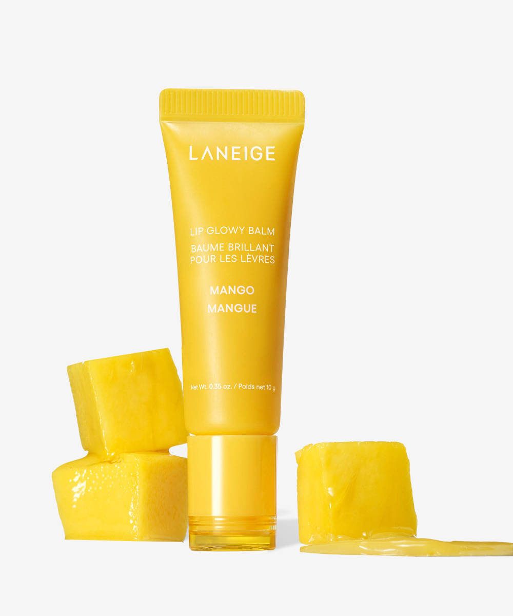A yellow tube of LANEIGE Lip Glowy Balm - Mango 10g stands upright, surrounded by three fresh mango cubes on a plain white background. One cube in the foreground has juice pooling around it, highlighting the balms rich hydration.