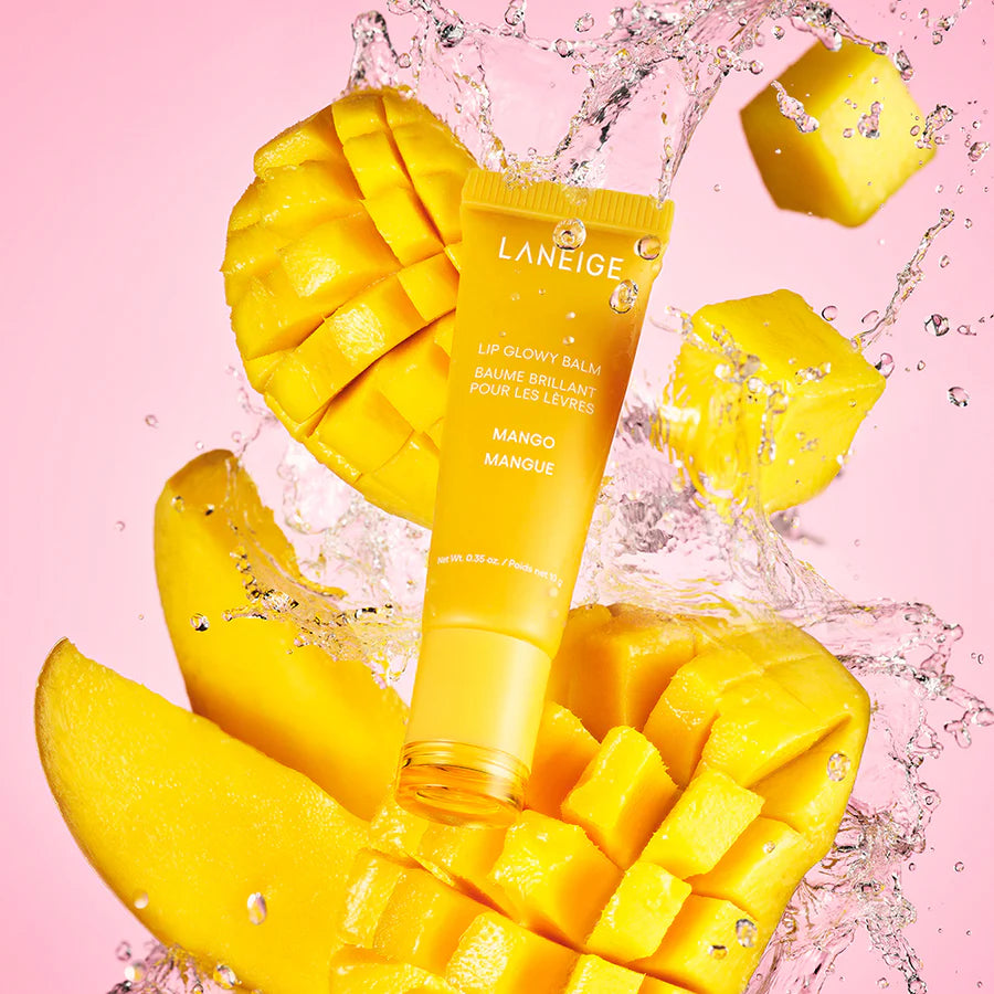 A Laneige Lip Glowy Balm - Mango 10g from LANEIGE, known for intense hydration, is displayed alongside fresh mango slices and splashes of water on a pink backdrop.