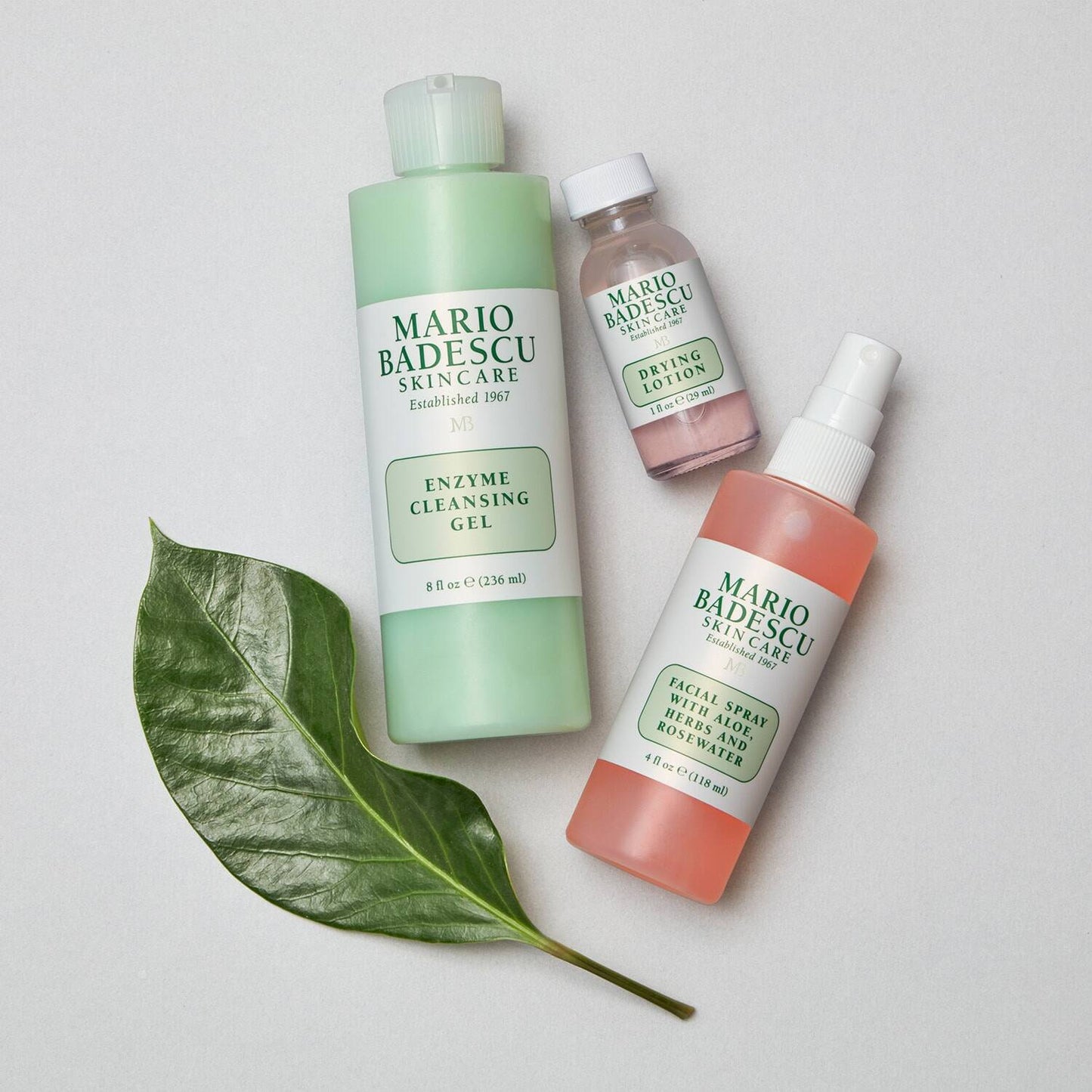 Three Mario Badescu skincare products on a light background with a green leaf.