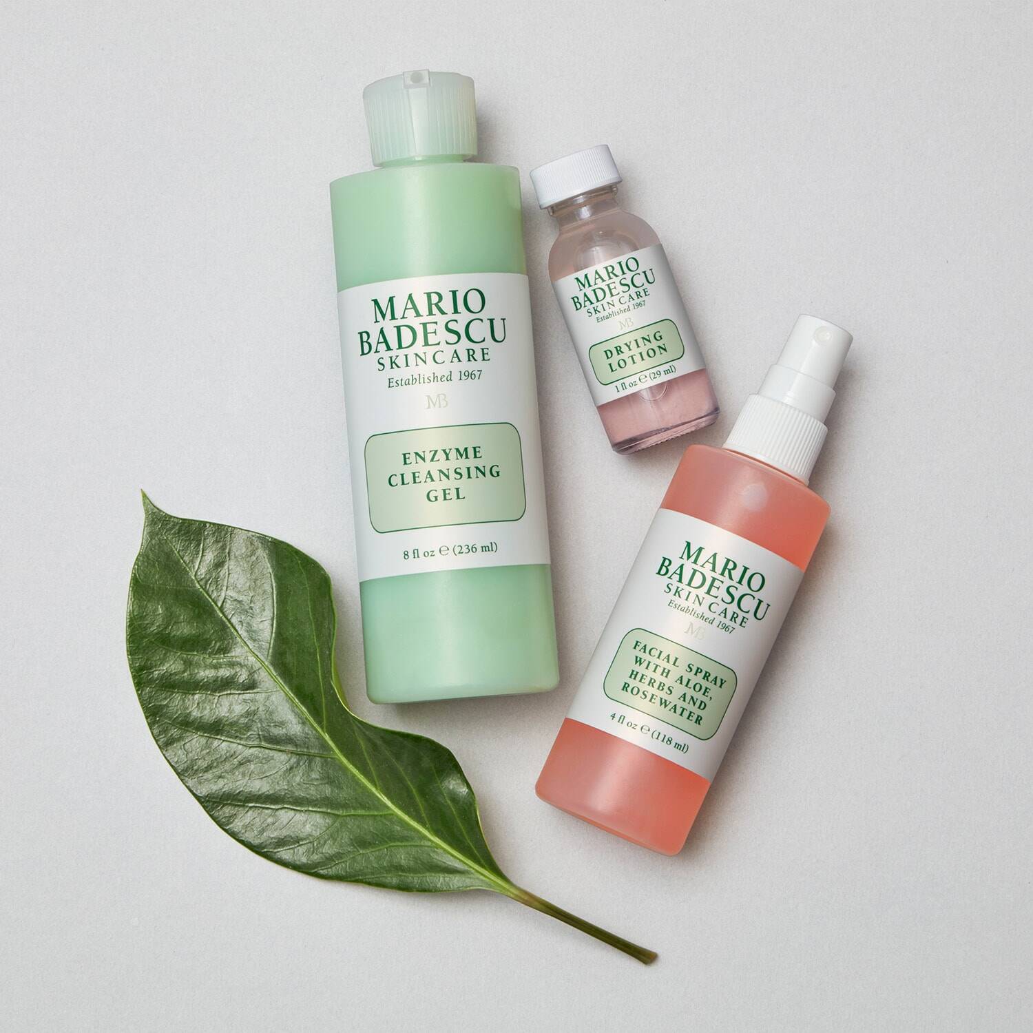 Three Mario Badescu skincare products on a light background with a green leaf.