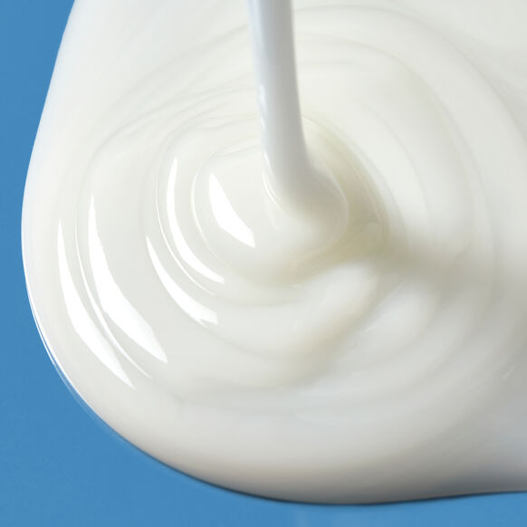 A close-up of Naturium The Energizer Mandelic Acid Body Wash 500ml, by Naturium, being poured onto a smooth blue surface, forming swirling patterns as the creamy white formula spreads.