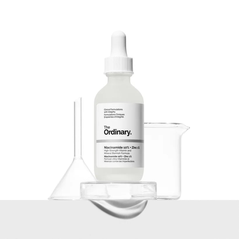 A 30ml bottle of The Ordinary Niacinamide 10% + Zinc 1% is displayed against a white background, ideal for blemish-prone skin. It accompanies a clear funnel and beaker on a clean surface, highlighting the serums niacinamide and zinc PCA benefits.