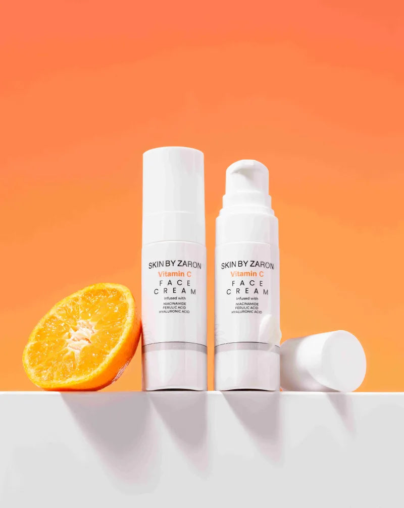 Two skincare bottles with a sliced orange on an orange background