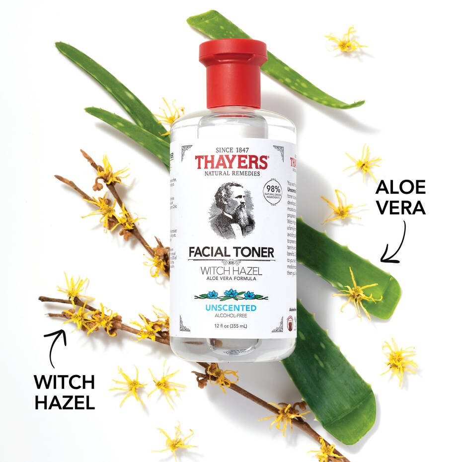 A bottle of THAYERS Facial Toner - Witch Hazel Aloe Vera Formula-Unscented 355ml is nestled on a white background with fresh leaves, showcasing its natural ingredients and confirming its unscented and alcohol-free.