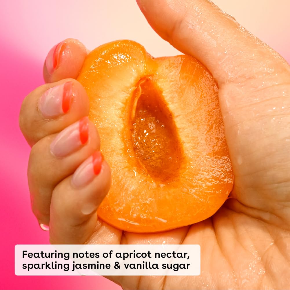 A hand holds a juicy apricot half against a pink background. The bright orange fruit with its textured pit teases the senses, while text reads, Notes of apricot nectar, sparkling jasmine & vanilla sugar, perfect for sensitive skin in eos Shea Better 24H Moisture Body Lotion - Jasmine Peach (473ml).
