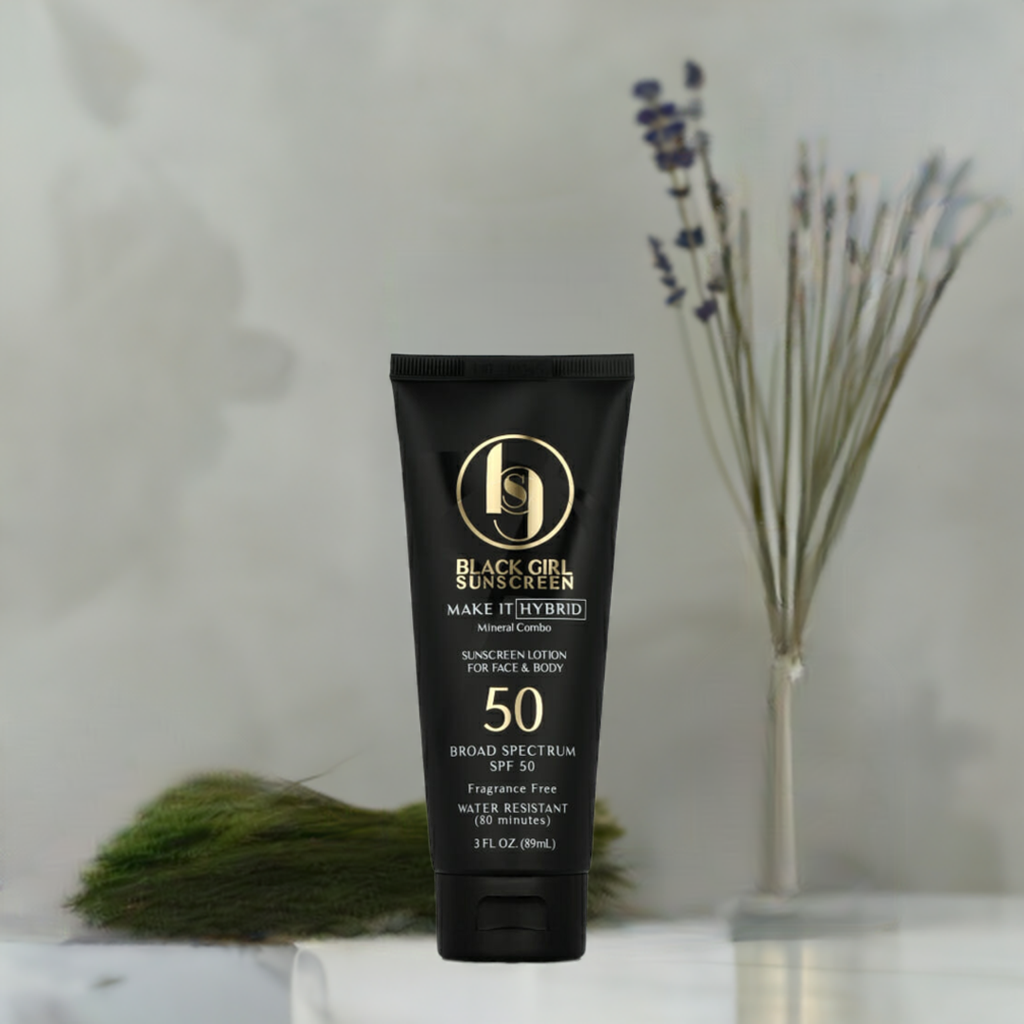 An 89ml tube of Black Girl Sunscreen Make It Hybrid™ SPF50 with moisturizing ingredients stands on a surface, against a blurred lavender and green foliage background. The sleek black and gold packaging highlights its broad-spectrum, fragrance-free protection.
