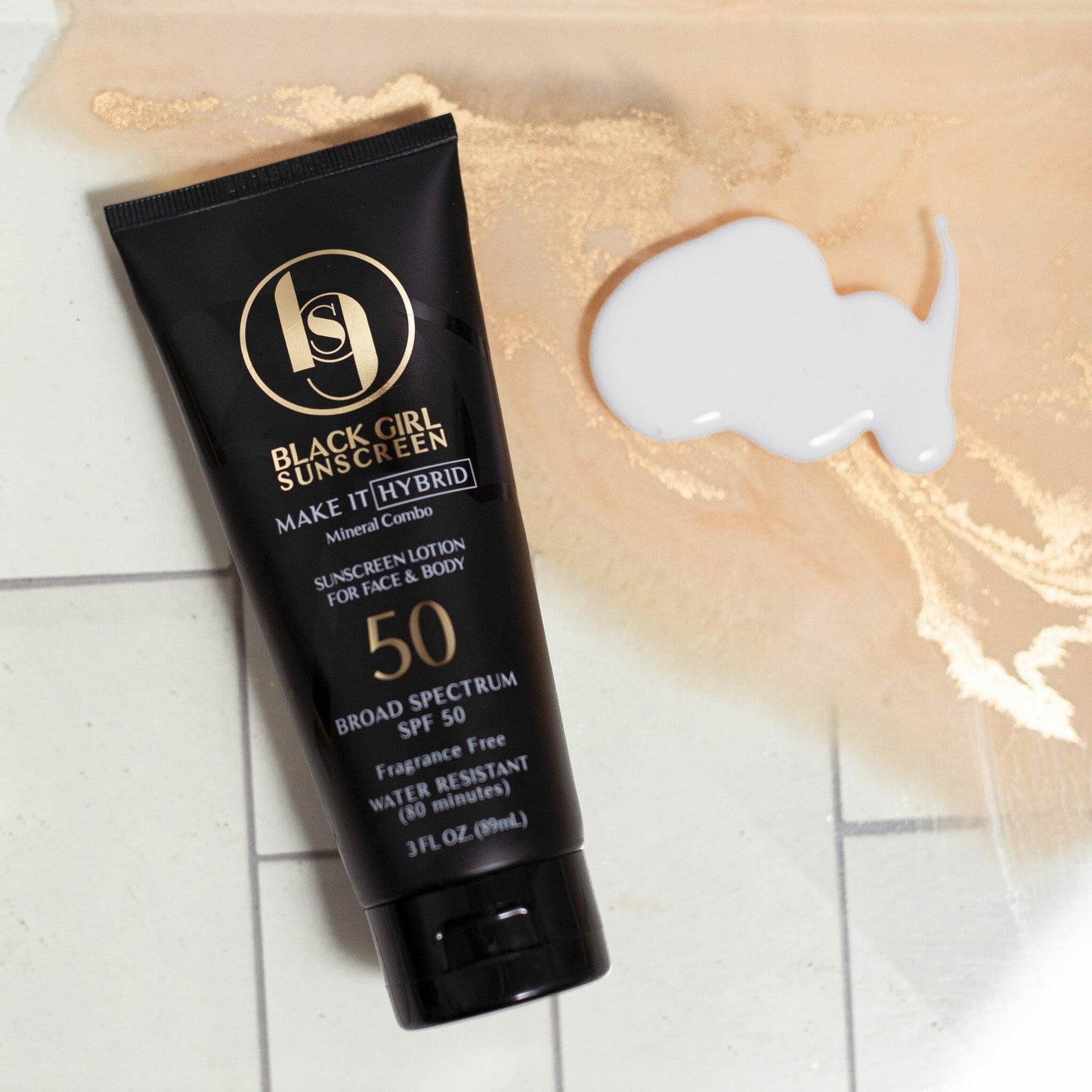 A tube of Black Girl Sunscreen Make It Hybrid™ SPF50 - 89ml, a broad-spectrum, fragrance-free sunscreen with a mineral and synthetic formula, rests on a surface with white lotion spilled nearby. Its water-resistant for 80 minutes.