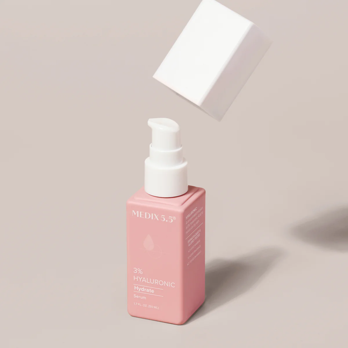 A pink bottle of Medix 5.5, 3% Hyaluronic Acid Hydrate Serum (1.7 fl oz) with a white pump appears on a beige background. Its floating white cap suggests its recently removed or about to be replaced, promising hydration enhanced by Vitamin B5.