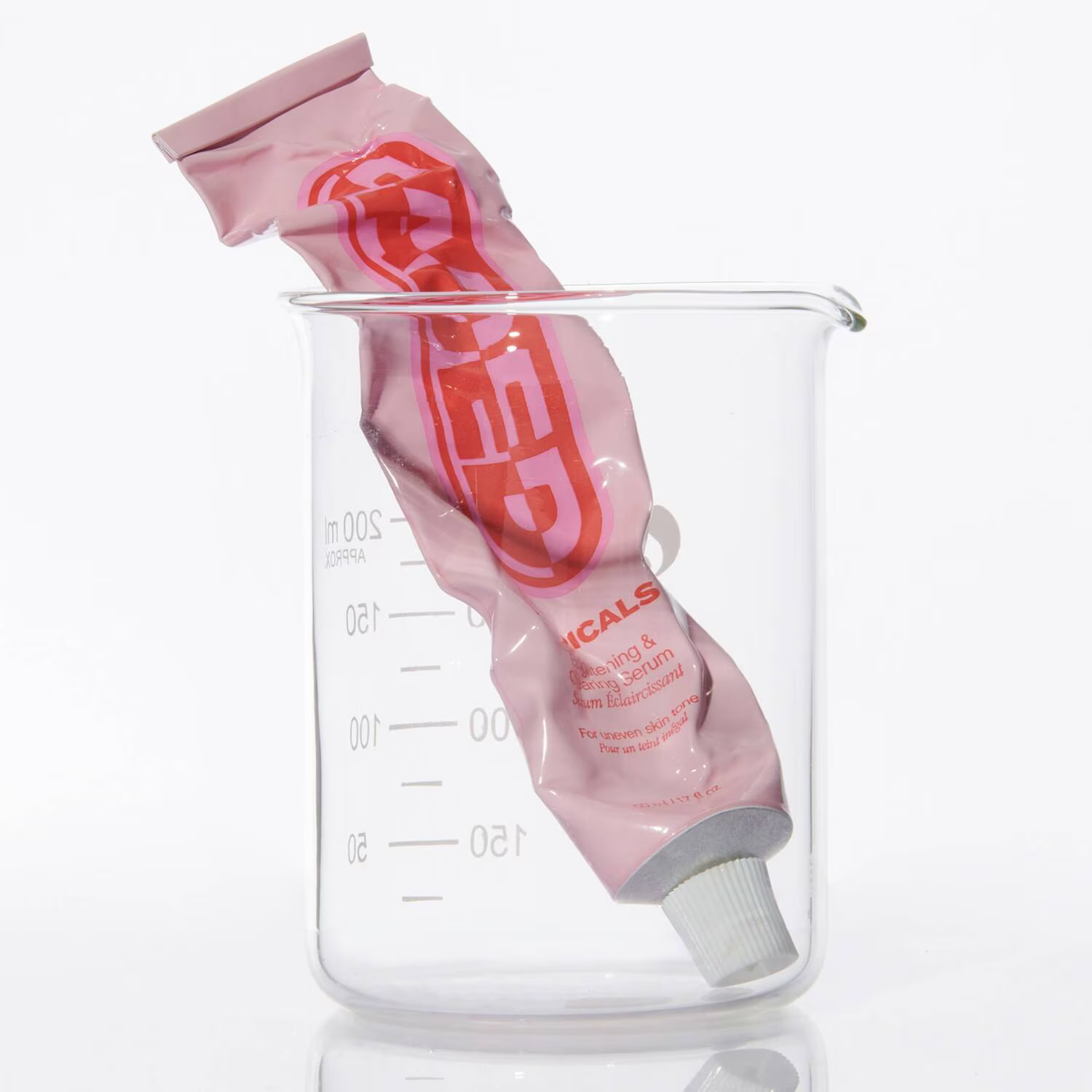 A pink tube, labeled Topicals Faded Brightening and Clearing Serum 50ml from TOPICALS, rests inside a transparent glass beaker with measurement markings. The red-capped tube stands elegantly against a plain white backdrop.