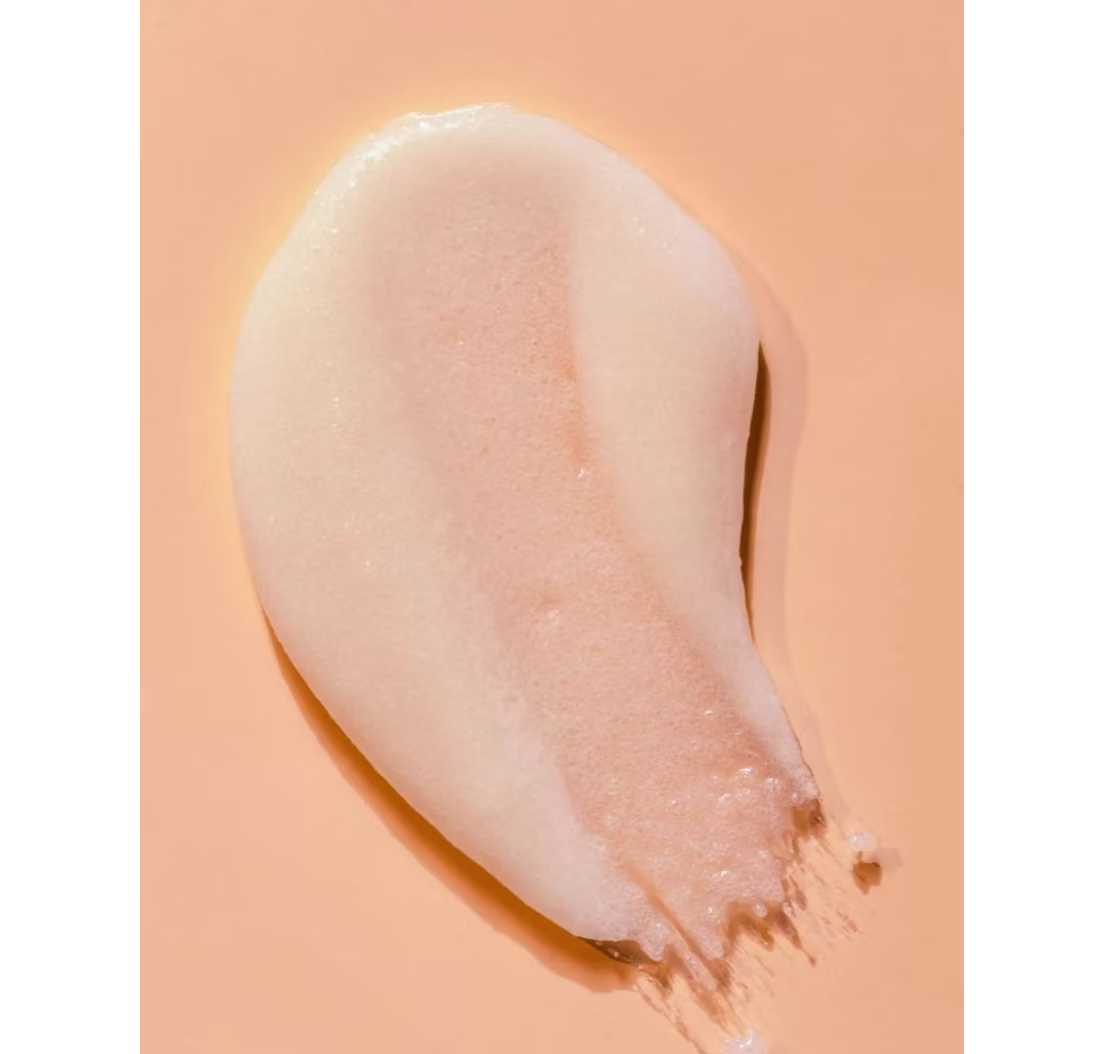 A blob of Tree Huts smooth, glossy Shea Sugar Body Scrub, infused with shea butter and featuring a creamy vanilla texture, spread on a peach-colored background.