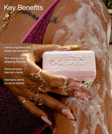 A person with manicured nails and gold jewelry lathers the Topicals Faded Cleansing Bar on their arm. The overlay text lists key benefits: gently brightens and fades discoloration, non-drying formula, reduces post-blemish marks, and maintains the skin’s moisture barrier.