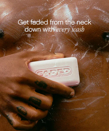 A close-up of a person using the Topicals Faded Cleansing Bar on their chest, creating a foamy lather. The text reads, 'Get faded from the neck down with every wash,' highlighting its brightening and exfoliating properties.