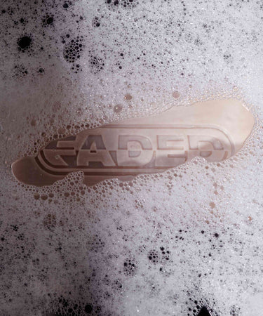 A Topicals Faded Cleansing Bar partially submerged in bubbly foam, with the word 'FADED' visible through the suds, emphasizing the cleansing experience.