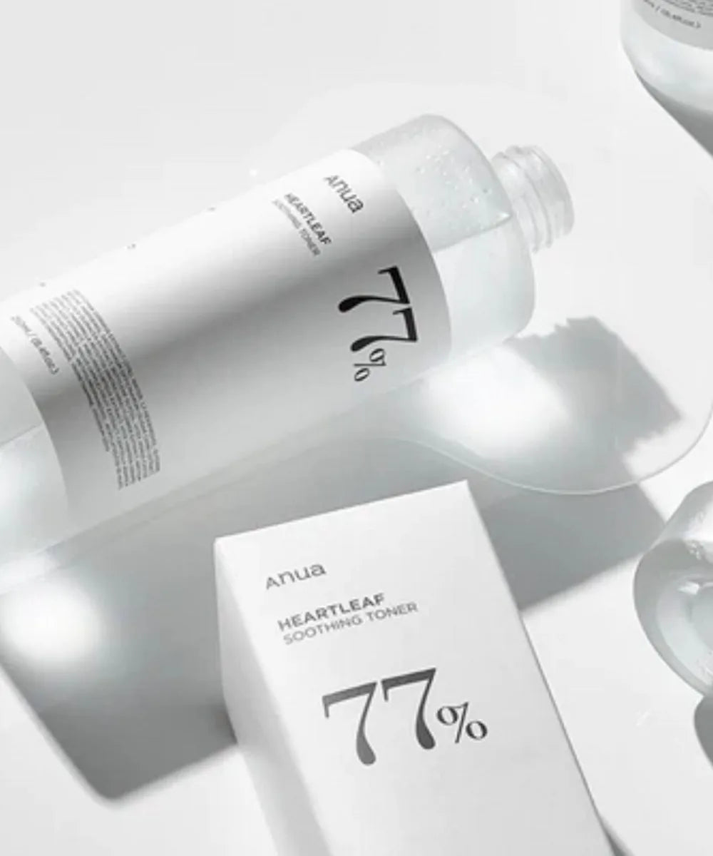 A clear bottle and a white box of ANUA Heartleaf 77% Soothing Toner 250ml, both with minimalist black text and a bold 77%, sit on a bright reflective surface. The toner is formulated with Houttuynia Cordata.