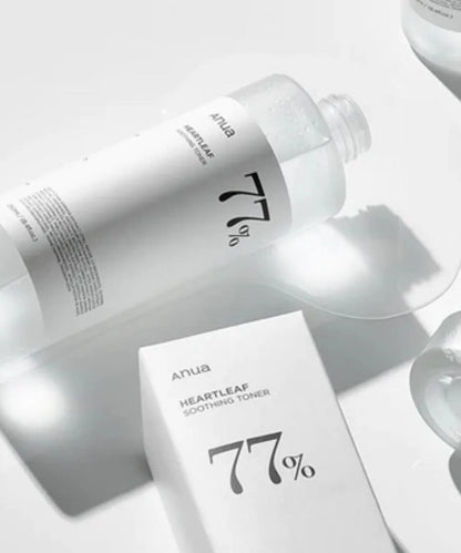 A clear bottle and a white box of ANUA Heartleaf 77% Soothing Toner 250ml, both with minimalist black text and a bold 77%, sit on a bright reflective surface. The toner is formulated with Houttuynia Cordata.