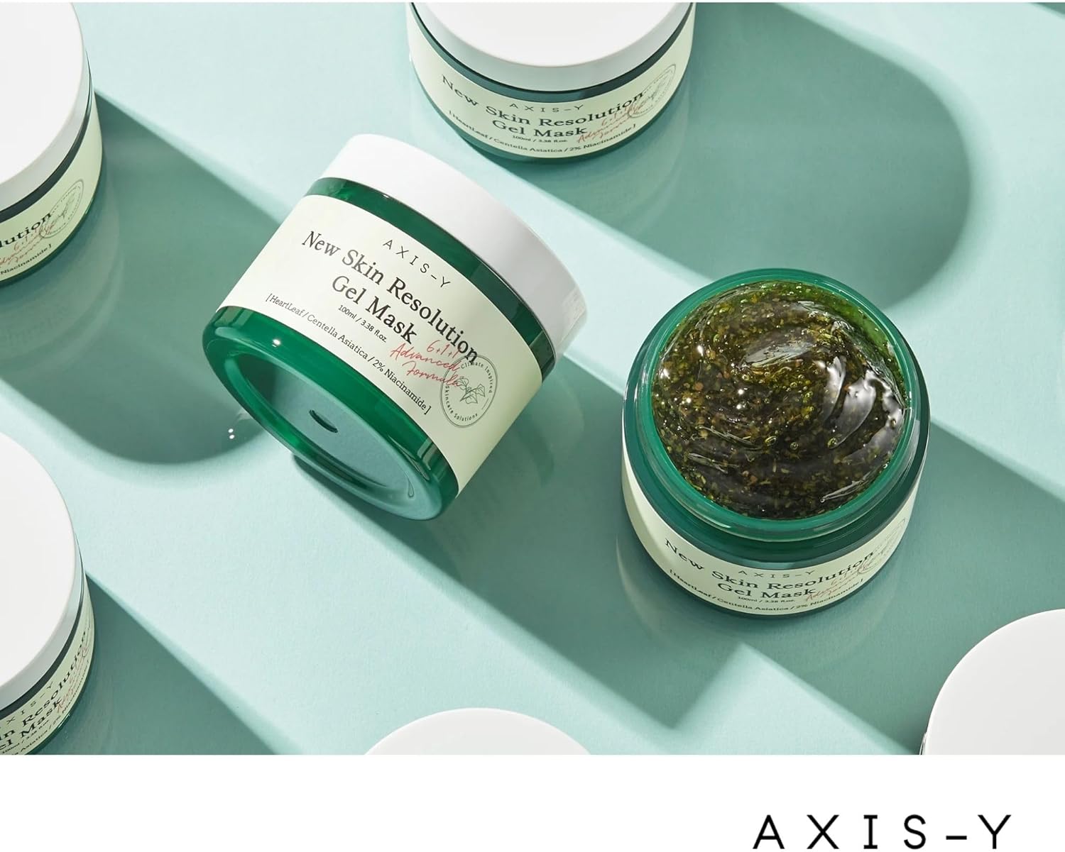 Jars of the Axis-Y New Skin Resolution Gel Mask 100ml are displayed on a light green surface. One jar is open, showcasing the soothing green gel with niacinamide and natural ingredients. The label emphasizes key benefits and ingredients.
