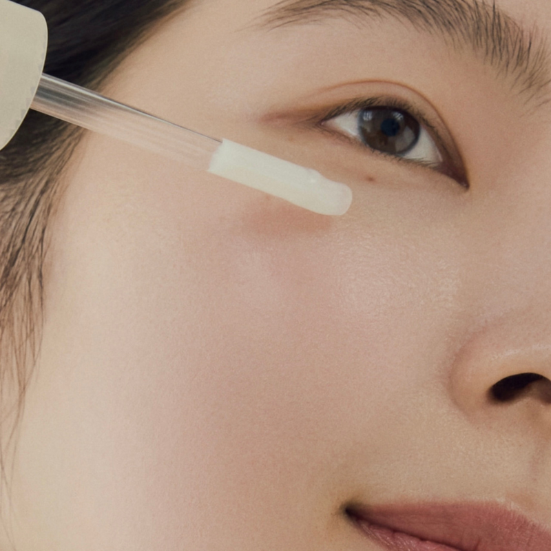 Close-up of a woman's face with a dropper applying ABIB Jericho Rose Bifida Serum near her eye, highlighting the serum's smooth texture and hydration benefits.