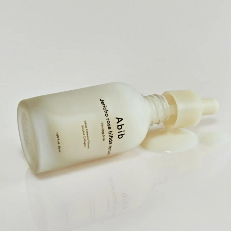 ABIB Jericho Rose Bifida Serum Firming Drop 50ml bottle lying on its side with the dropper removed, showing spilled serum, highlighting its smooth texture.