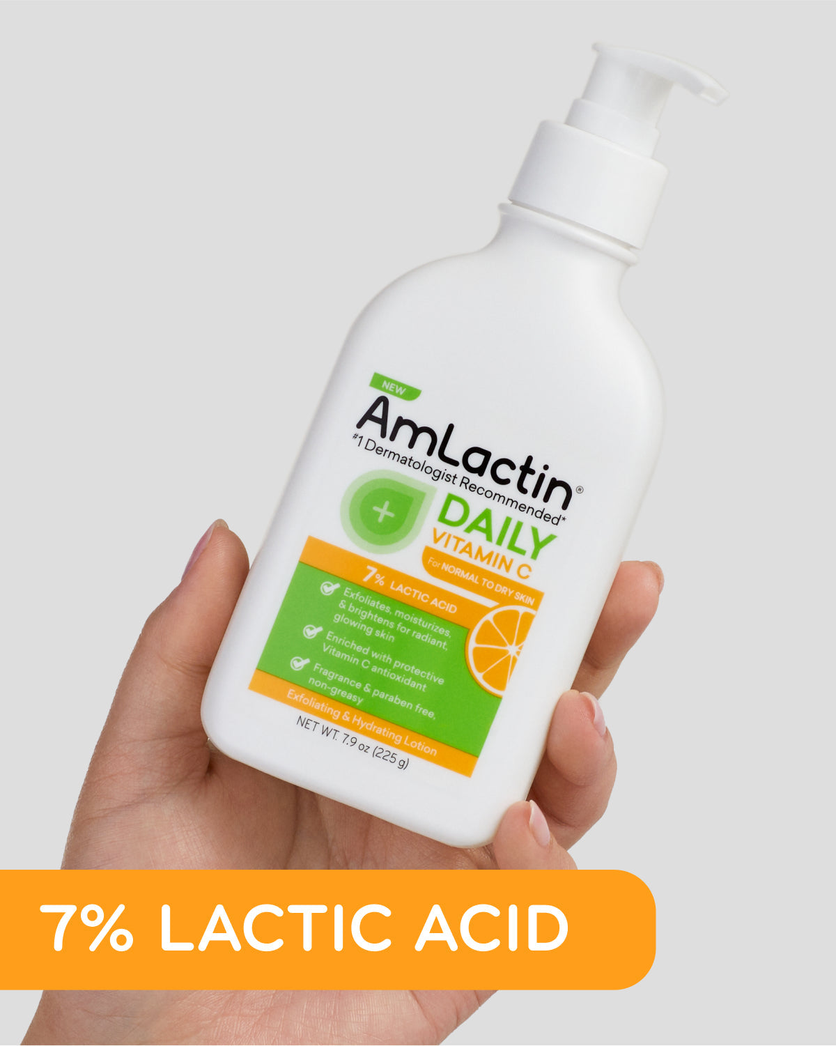 A hand holds a white AmLactin Daily Vitamin C Lotion 7% Lactic Acid (225g) bottle. The label features orange and green accents, with an orange banner at the bottom highlighting 7% LACTIC ACID.