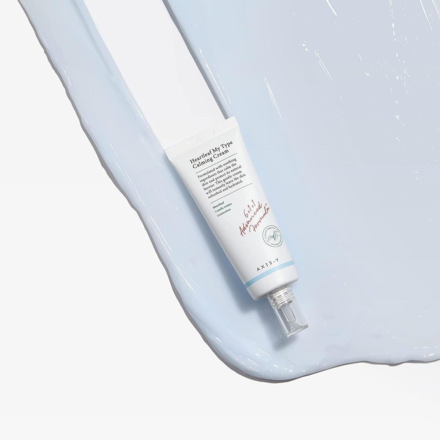 A tube of AXIS-Y Heartleaf My Type Calming Cream 60ml rests on a textured surface with a light blue cream swatch. The design is simple, with text and a transparent cap.