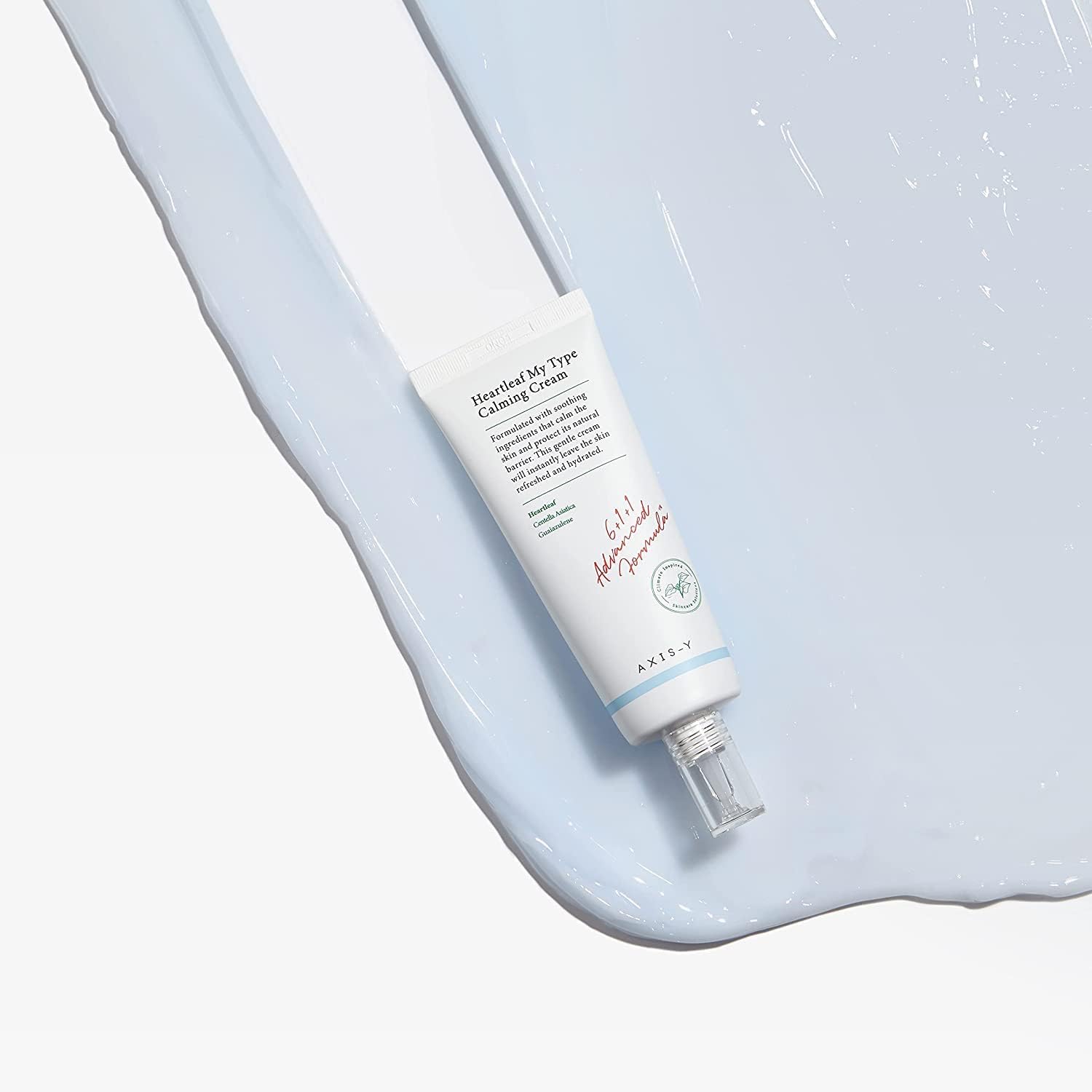 A tube of AXIS-Y Heartleaf My Type Calming Cream 60ml rests on a textured surface with a light blue cream swatch. The design is simple, with text and a transparent cap.
