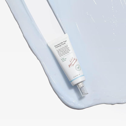 A tube of AXIS-Y Heartleaf My Type Calming Cream 60ml rests on a textured surface with a light blue cream swatch. The design is simple, with text and a transparent cap.