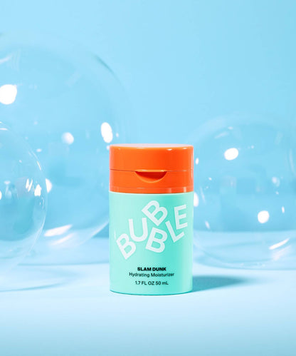 A mint green bottle with an orange cap shows Bubble Slam Dunk Hydrating Moisturiser Cream 50ml against a blue background, surrounded by large transparent bubbles. Infused with soothing Aloe Leaf Juice, this moisturizer adds a refreshing touch to your skincare regimen.