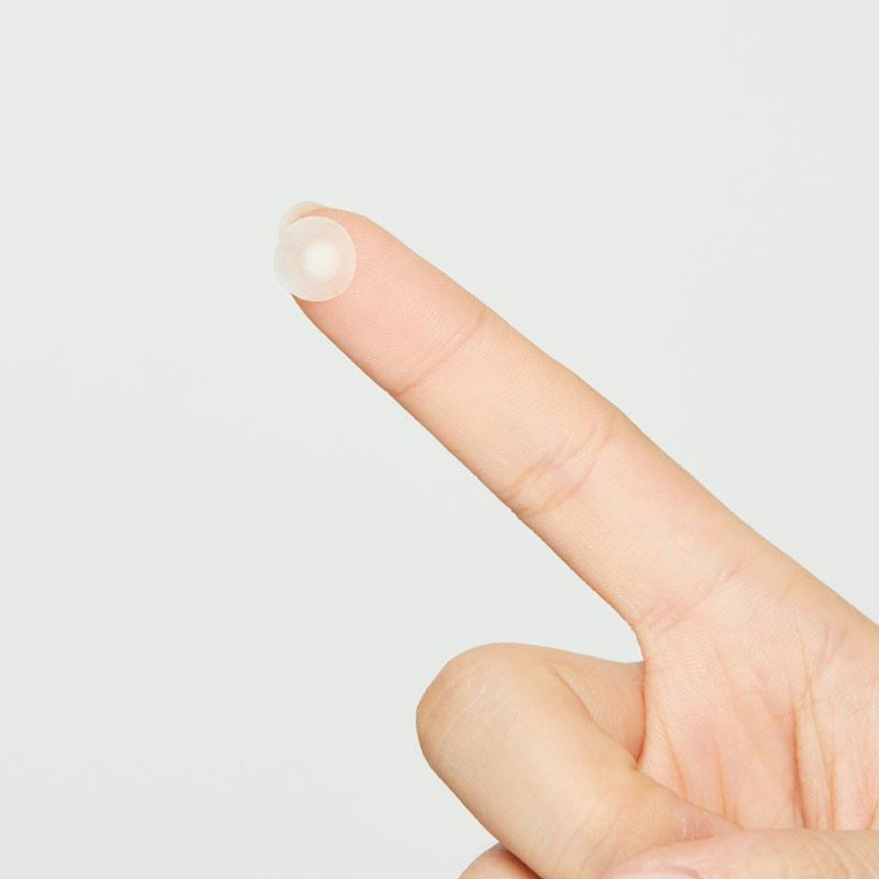 Close up of a COSRX Acne Pimple Patch on a fingertip. A hydrocolloid patch designed to absorb impurities, protect blemishes, and speed up acne healing.