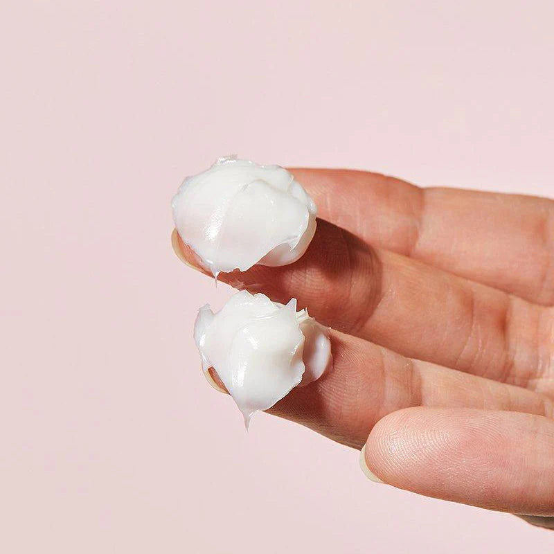 Two white coconut halves held between fingers against a pink background