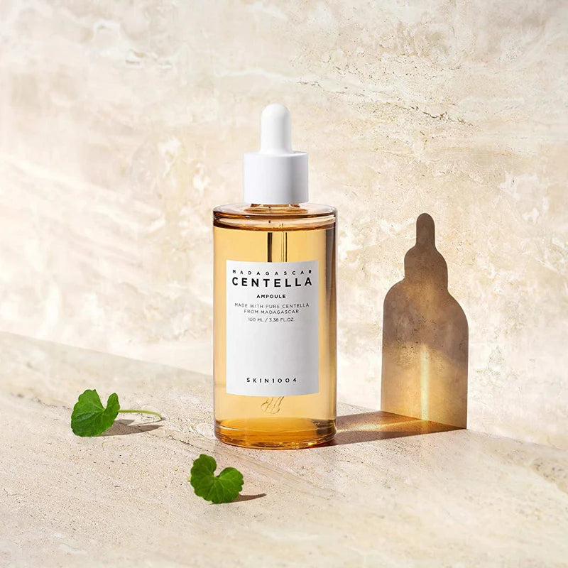 SKIN1004 Madagascar Centella Ampoule bottle on a textured surface with sunlight casting a dropper-shaped shadow, surrounded by Centella leaves.