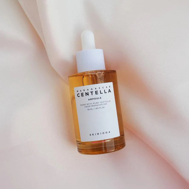 SKIN1004 Madagascar Centella Ampoule bottle with a dropper cap, placed on soft, silky fabric. The golden liquid contrasts with the smooth, elegant backdrop.