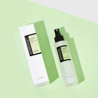 A bottle of COSRX Centella Water Alcohol-Free Toner rests on a light green surface with its white and green packaging box. The background shifts diagonally from light green to nearly white, enhancing the tranquil vibe of this soothing skincare essential.