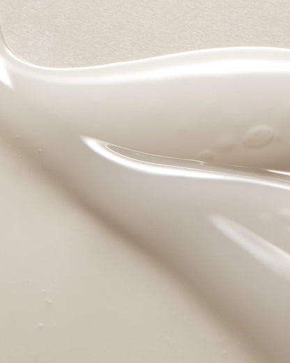 A close-up image reveals a smooth, creamy beige liquid with soft waves and light reflections, representing the fluidity of the AXIS-Y Dark Spot Correcting Glow Serum 50ml by AXIS-Y—an ideal choice for diminishing dark spots and enhancing your glow.