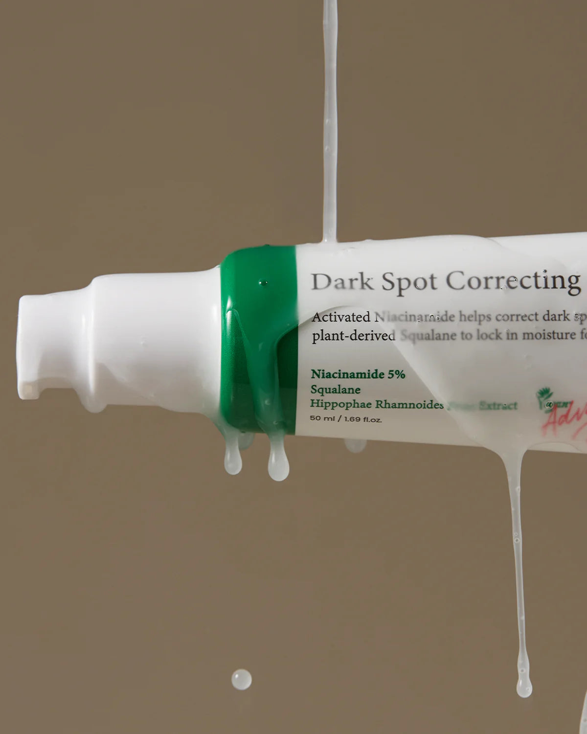A 50ml white tube of AXIS-Y Dark Spot Correcting Glow Serum, featuring green accents, hangs with creamy liquid dripping. The label emphasizes Niacinamide, Squalane, and Hippophae Rhamnoides extract for dark spot correction against a brown background.