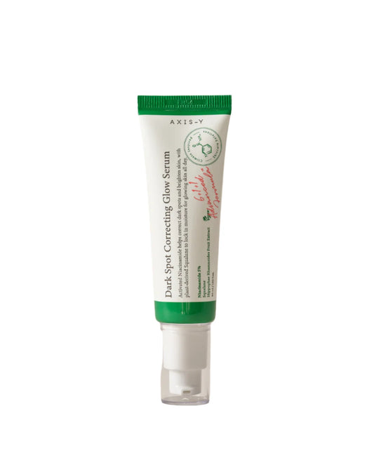 A small tube with a green cap contains AXIS-Y Dark Spot Correcting Glow Serum 50ml, enriched with niacinamide. The white tube features green and red text, minimalist design elements, and product information on the label.