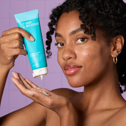 Woman applying cream from a 'Good Molecules' tube against a purple background