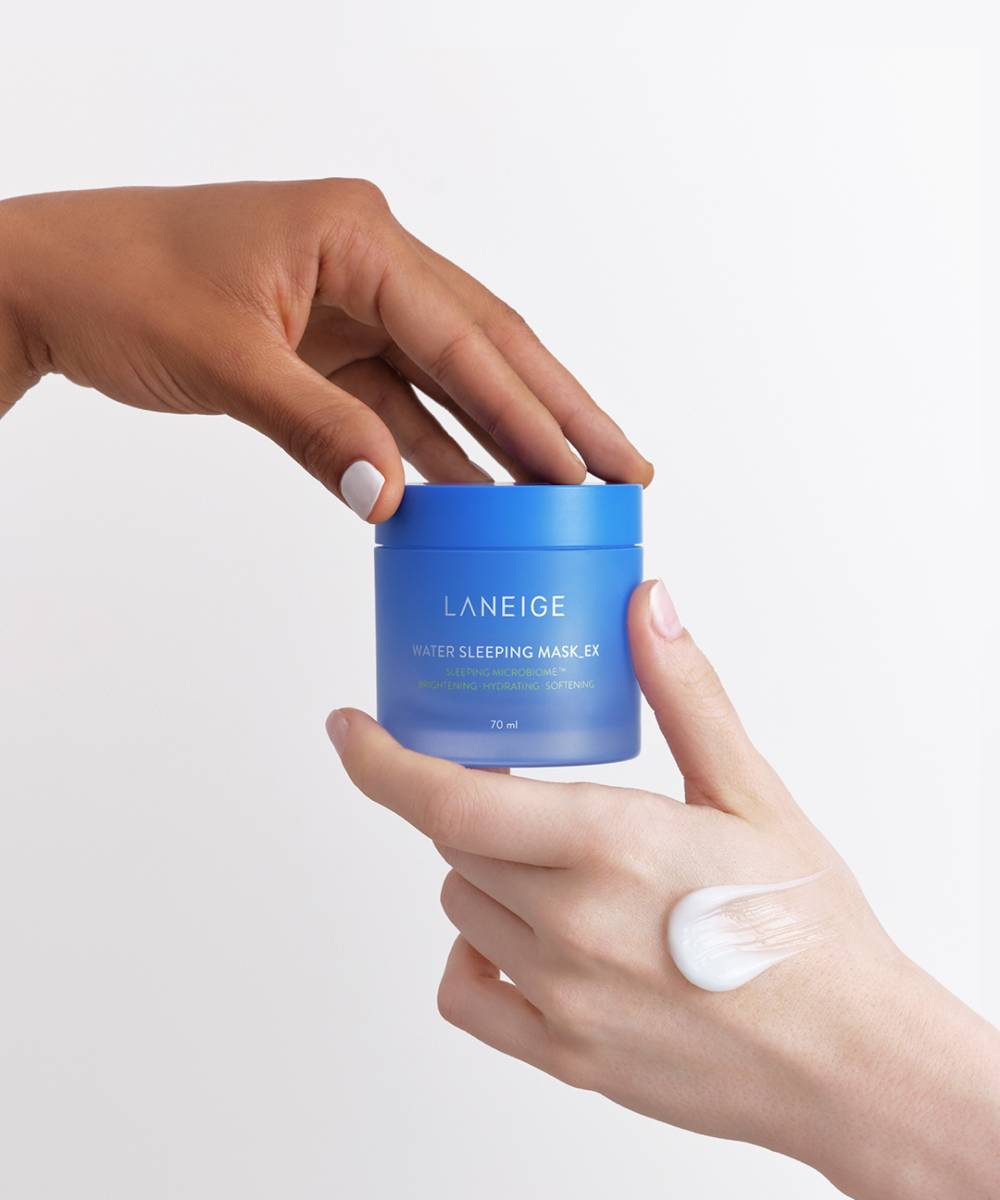 Two hands appear: one holds a blue 70ml container of LANEIGE Water Sleeping Mask, an ideal hydrating overnight mask, while the other displays a dab of cream on the back. The background is plain white.