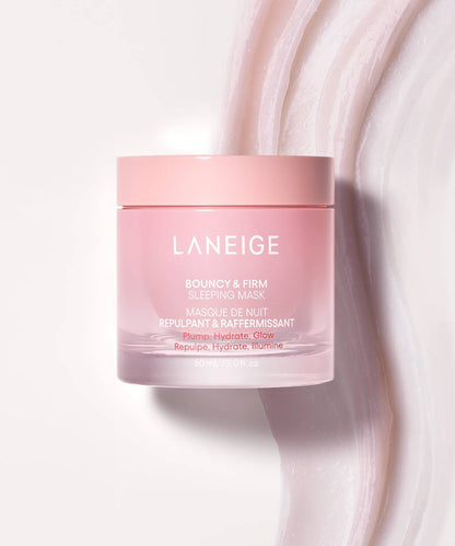 A jar of LANEIGE Bouncy & Firm Sleeping Mask sits on a marbled pink and white surface. This pink jar, featuring white text, promises to plump, hydrate, and illuminate for optimum skin radiance. Capacity is 60 ml (2.0 fl. oz.).