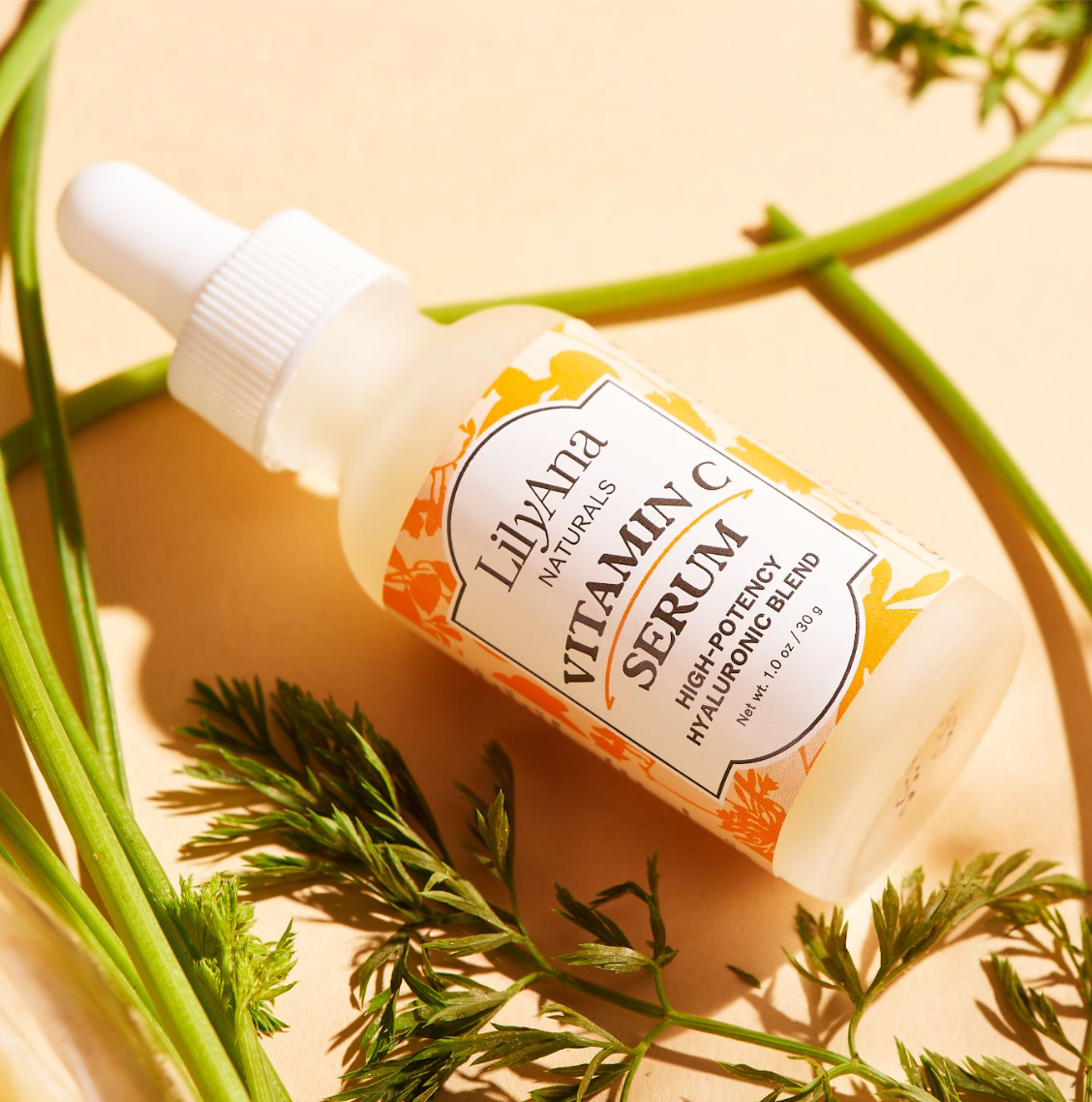 LilyAna Naturals Vitamin C Serum bottle with dropper on a beige background with green leaves.