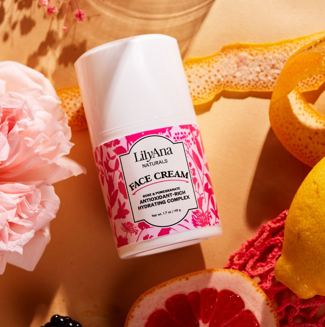 LilyAna Naturals face cream bottle with pink floral design on a textured surface with fruits and flowers.