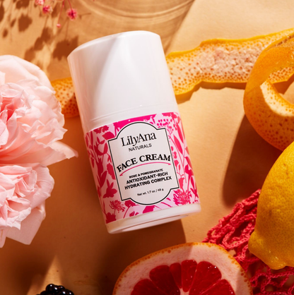 LilyAna Naturals face cream bottle with pink floral design on a textured surface with fruits and flowers.