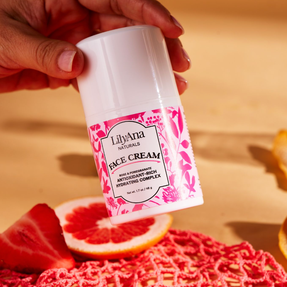 Hand holding a container of LilyAna Naturals face cream with a pink floral design on a wooden surface.