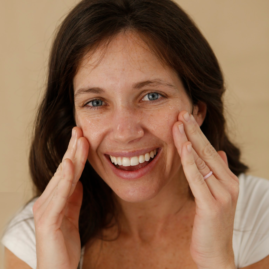 Woman smiling and touching her cheeks against a beige background