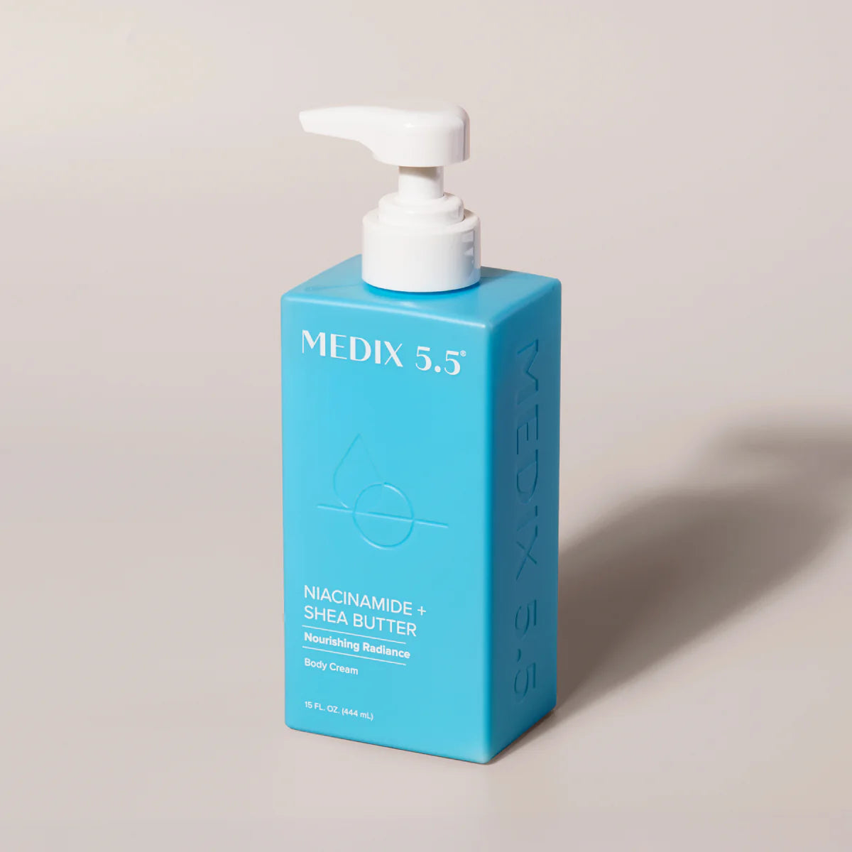 A blue rectangular pump bottle labeled MEDIX 5.5, featuring the new Medix 5.5 Niacinamide + Shea Butter Body Cream, is photographed on a neutral background.