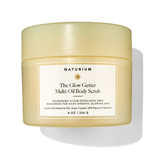 A jar of Naturium The Glow Getter Multi-Oil Body Scrub, featuring a pale yellow translucent container and a cream-colored label with black text, set against a clean white background with a soft shadow.