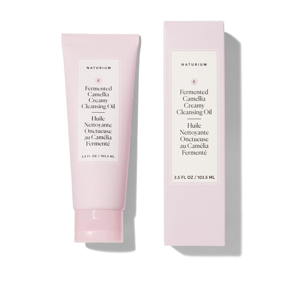 A pale pink skincare tube and matching rectangular box for Naturium Fermented Camellia Creamy Cleansing Oil, shown on a clean white background with soft shadows.
