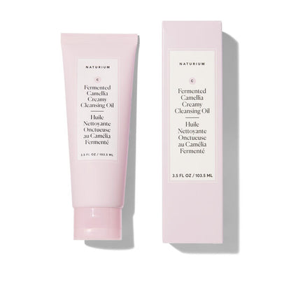 A pale pink skincare tube and matching rectangular box for Naturium Fermented Camellia Creamy Cleansing Oil, shown on a clean white background with soft shadows.